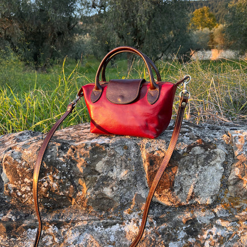 Floto Gattane Red handbag with brown strap on a stone wall in a natural setting