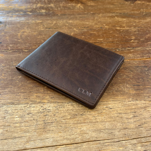 Brown leather wallet with initials on a wooden surface