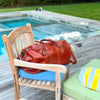 Brown leather duffel bag on a wooden chair by a poolside.