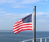 American flag waving on a boat with a clear blue sky and water background