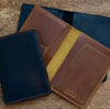 Three leather wallets in brown, black, and blue on a wooden surface