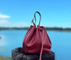 Red leather bucket bag on a wooden post with a blurred lake and sky background