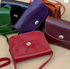 Four leather handbags in different colors arranged on a light surface.
