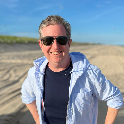 Man wearing sunglasses and a light blue jacket on a beach