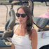 Woman wearing sunglasses and a white top in front of a golf cart.