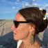Woman on a beach with sunglasses and a hair clip, looking to the side.